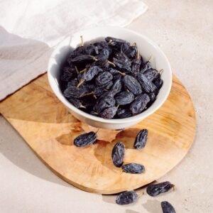 Dried black raisins in a white bowl on a wooden board
